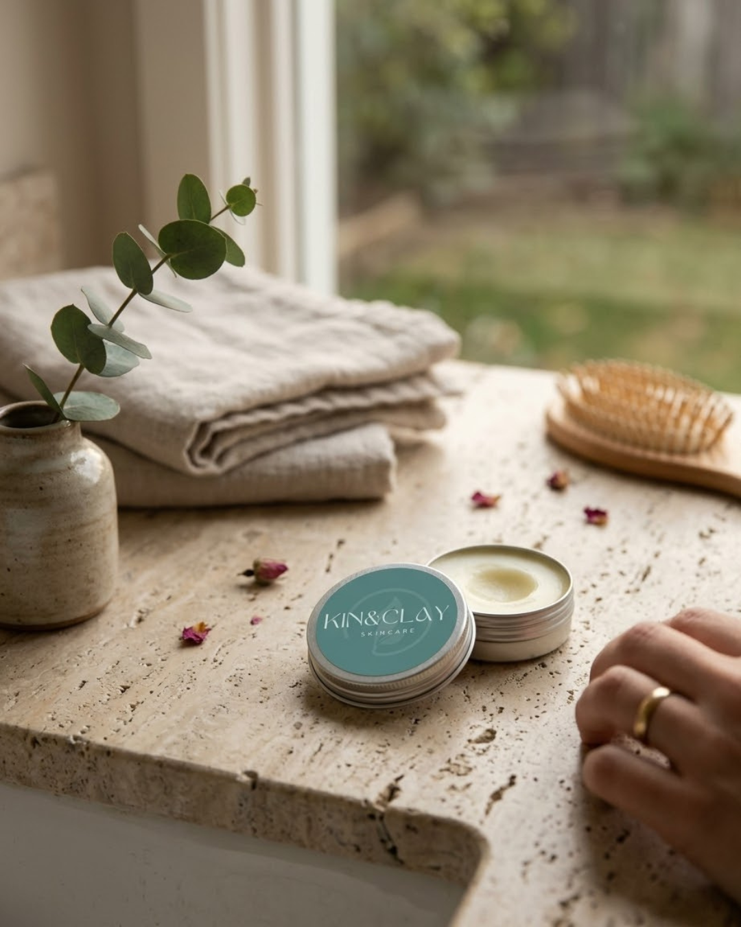 Open tin of Kin & Clay Coconut Lip Balm showing the balm texture, styled with eucalyptus and rose petals